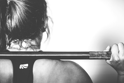 Monochrome image of a woman's back holding a barbell